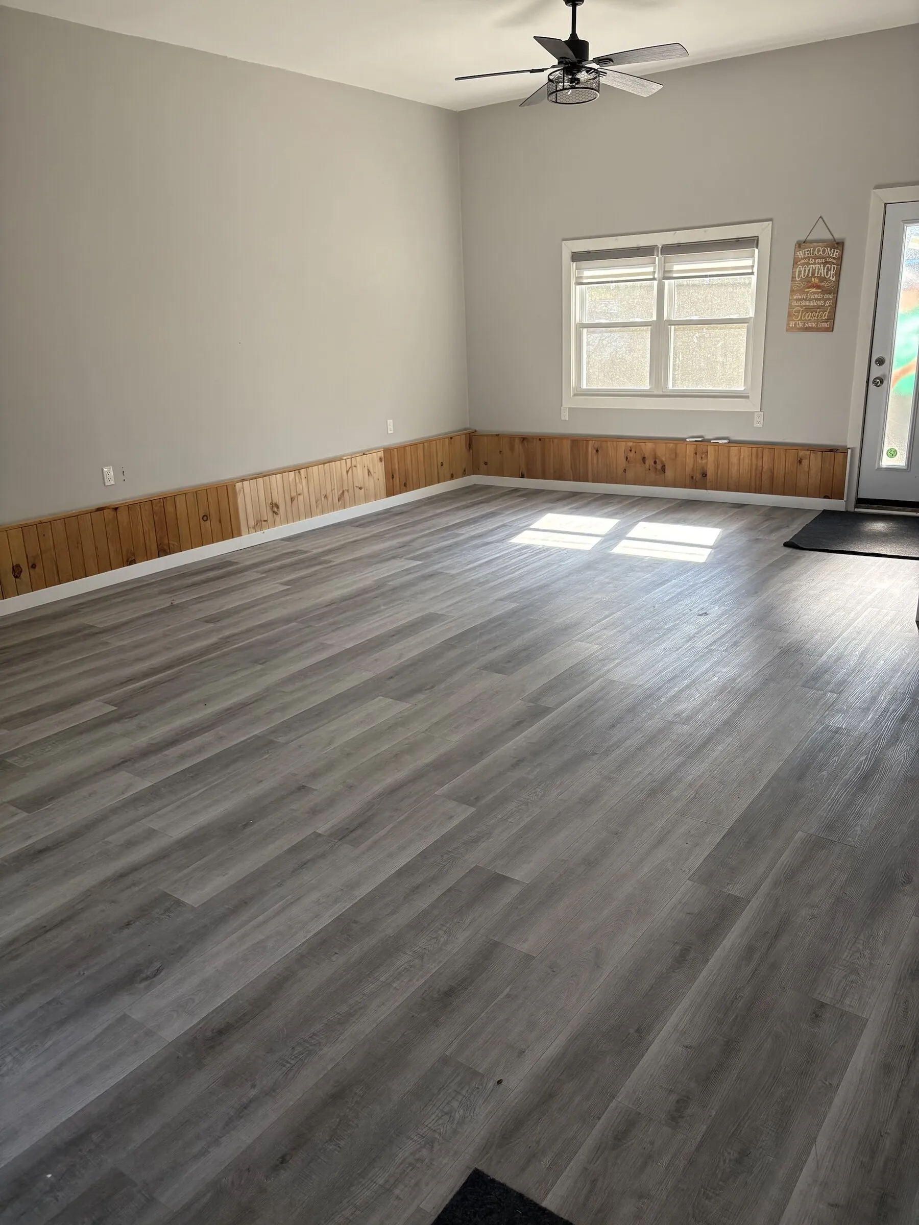 Large open Gathering Room with grey plank floor, pine wainscoting and ceiling fan